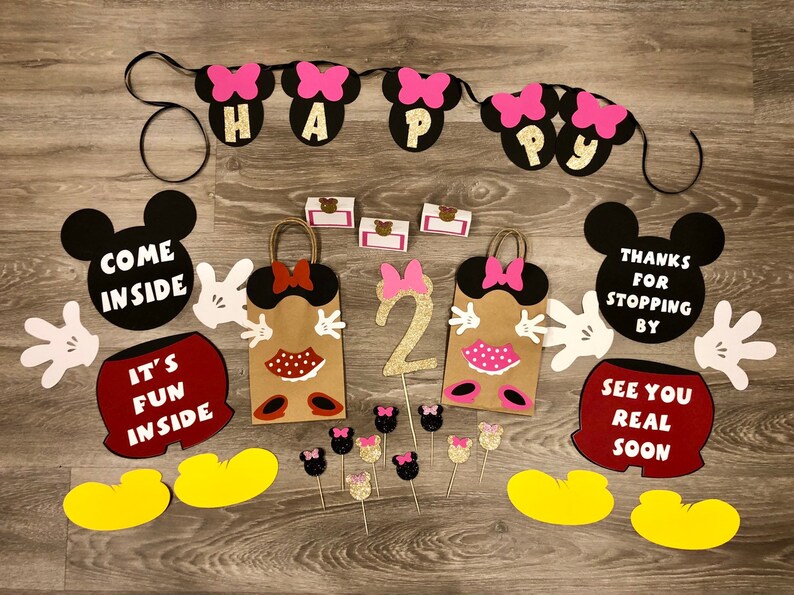 May include: A set of Mickey Mouse themed party decorations, including a banner with the words "Happy", two Mickey Mouse head cutouts with the text "Come Inside" and "Thanks for Stopping By", two brown paper bags with Mickey Mouse ears and bows, and a number two with glitter.