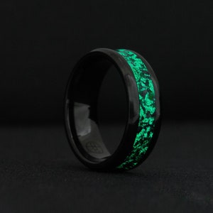 Pode incluir: Um anel preto com uma banda verde que brilha no escuro. O anel é feito de um material durável e tem um acabamento liso.
