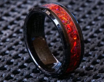 May include: A black ceramic ring with a red and orange inlay. The ring has a polished finish and a beveled edge.