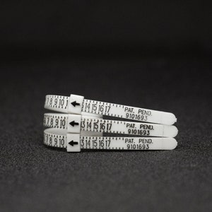 Pode incluir: Tr&ecirc;s calibradores de anel de pl&aacute;stico branco com marcas e flechas pretas. Os calibradores s&atilde;o etiquetados com n&uacute;meros de 7 a 17 e o texto "PAT. PEND. 9101693".