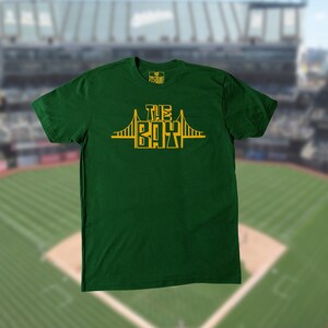 May include: A green t-shirt with a yellow graphic of the Golden Gate Bridge and the text "The Bay" on the front.