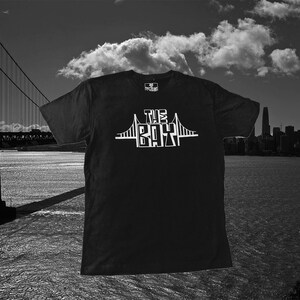 May include: Black t-shirt with a white graphic of the Golden Gate Bridge and the text "The Bay" on the front.