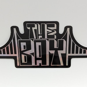 May include: Black and silver sticker with the text "THE BAY" and a silhouette of the Golden Gate Bridge.