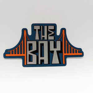 May include: A blue and orange sticker with the text "THE BAY" and a stylized image of the Golden Gate Bridge.