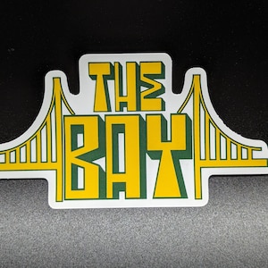 May include: A white sticker with a green and yellow graphic of the Golden Gate Bridge and the text "THE BAY".