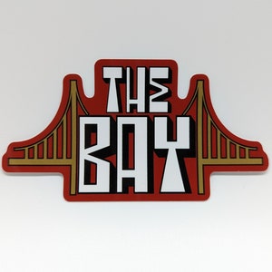 May include: Red and gold sticker with the text "THE BAY" and a stylized image of the Golden Gate Bridge.