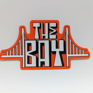 May include: Orange sticker with a white outline of the Golden Gate Bridge and the text "THE BAY" in black and white.