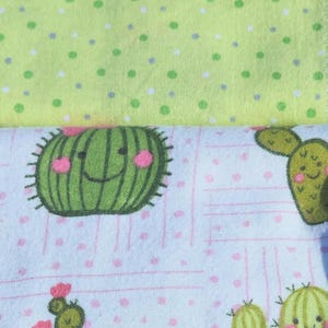 May include: A white fabric with a pink and green cactus pattern. The cactus has a smiling face and pink cheeks. The fabric has a light green polka dot pattern on the top.