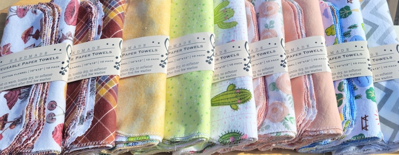 May include: Ten stacks of handmade reusable paper towels with various colourful patterns, including cacti, flowers, and geometric designs. Each stack has a label that reads "Handmade Reusable Paper Towels 10" x 10" / 10 in pack.  Wash, wring, dry, and use again and again.  No softener.