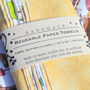 May include: A stack of 10 handmade reusable paper towels made from 100% cotton flannel. The towels are yellow and white with a brown label that reads "HANDMADE REUSABLE PAPER TOWELS 100% COTTON FLANNEL | 10"x12" | 10 PACK wash on warm, tumble dry, no softener more absorbent after first few washes".