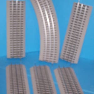 May include: A collection of model train tracks, including straight and curved sections. The tracks are gray with silver rails, set against a blue background. The pieces are made of plastic and are designed for a model train set.