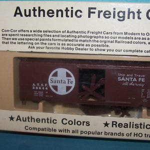 May include: A Con-Cor HO scale model railroad boxcar with a Santa Fe logo and lettering. The boxcar is painted brown with white lettering and a red cross. The boxcar is compatible with all popular brands of HO trains.