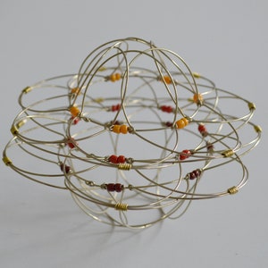 Puede incluir: Una escultura de esfera de alambre con un diseño geométrico. La esfera está decorada con pequeñas cuentas rojas y naranjas.