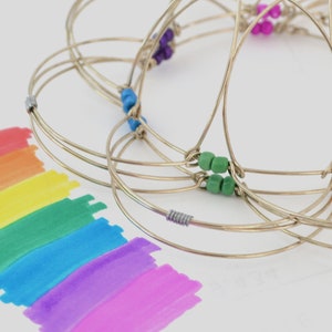 Puede incluir: Un rompecabezas de anillos de metal con cuentas de colores. El rompecabezas está hecho de múltiples anillos entrelazados, cada uno con una cuenta de color diferente. Las cuentas son verdes, naranjas, moradas y azules.