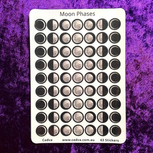 Puede incluir: Una hoja de pegatinas rectangular blanca titulada Moon Phases con 63 pegatinas circulares dispuestas en nueve filas de siete. Cada pegatina muestra una fase lunar diferente en tonos grises y negros. El texto inferior dice Cadva www.cadva.com.au 63 Stickers.