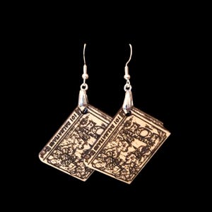 May include: A pair of rectangular drop earrings featuring a light-colored surface with a dark, detailed graphic print of 101 Dalmatians. The earrings are suspended from silver-toned metal fishhook wires and display the text 101 DALMATIANS.