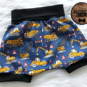 Peut inclure: Short de bébé à imprimé de véhicules de chantier bleus et jaunes avec une ceinture élastique noire. L'imprimé présente divers véhicules de chantier, notamment des camions à benne basculante, des excavateurs et des grues.
