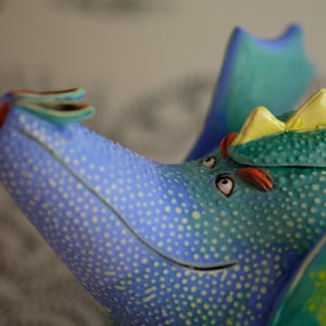 May include: A blue and green ceramic teapot shaped like a dragon with yellow accents and white polka dots.
