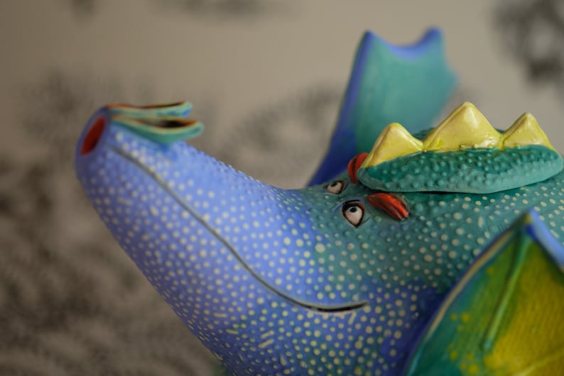 May include: A blue and green ceramic teapot shaped like a dragon with yellow accents and white polka dots.