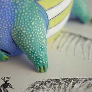 May include: A ceramic figurine with a blue, green, and yellow striped body. The figurine has a textured surface and a pointed tail.