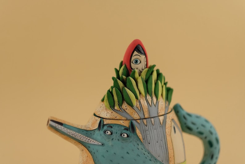 May include: A ceramic teapot with a wolf design and a red hooded girl peeking out from the top of the teapot.