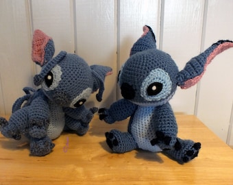 May include: Two blue crocheted Stitch plush toys from the Disney movie Lilo & Stitch. The toys are sitting on a wooden surface.