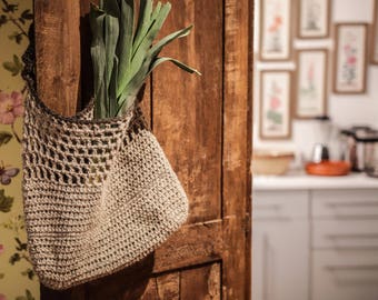 May include: A brown crocheted bag hanging on a wooden door with green leafy vegetables inside.
