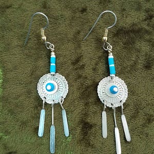 May include: A pair of silver earrings with blue and white accents. The earrings feature a circular design with a blue eye in the center and dangle with three silver strands.