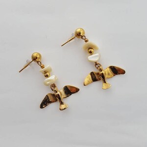 May include: Gold tone earrings with white shell beads and a bird charm.