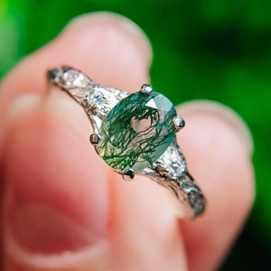 May include: A silver ring featuring a green moss agate gemstone. The ring has a delicate, intricate design with small accents.
