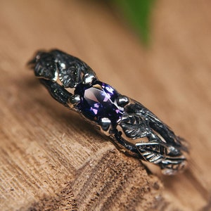 Könnte beinhalten: Ein silberner Ring mit einem violetten Edelstein, der in einem Blattdesign eingefasst ist. Der Ring liegt auf einer Holzoberfläche.