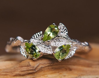 May include: A silver ring with three pear-shaped green gemstones set in a leafy design.