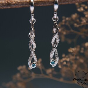 Può includere: Orecchini pendenti in argento con un design a ramo intrecciato e una piccola pietra preziosa blu alla fine di ogni orecchino.