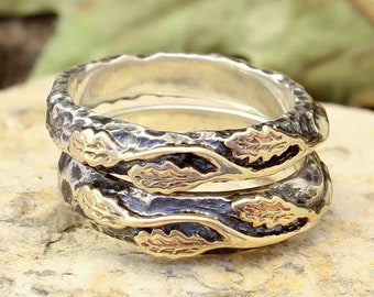 May include: Two silver wedding bands with a textured finish and gold leaf accents. The bands are stacked on top of each other and feature a design of leaves.