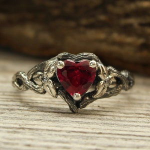 Peut inclure: Une bague en argent avec une pierre précieuse en rubis en forme de cœur sertie dans un motif de vigne torsadée.