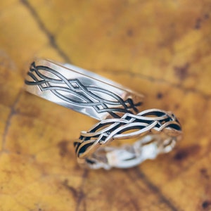 May include: Two silver wedding bands with a Celtic knot design. The bands are on a yellow leaf.