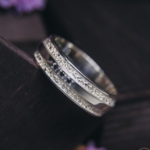 Może przedstawiać: Złota obrączka ślubna z fakturowanym wykończeniem i rzędem małych czarnych kamieni szlachetnych.