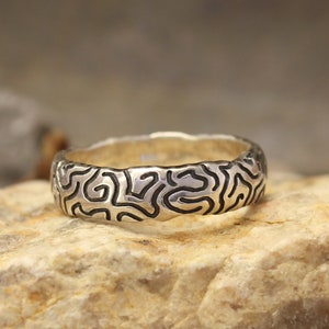 May include: A silver wedding band with a unique, organic, black and white patterned design.