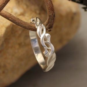 May include: A silver wedding band with a braided design. The band is on a rustic background.