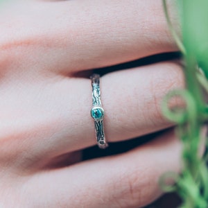 May include: A silver ring with a blue gemstone set in a textured band. The ring is worn on a finger.
