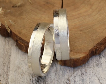 May include: Two silver wedding bands with a brushed finish. One band has a small diamond set in the center.