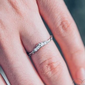 Könnte beinhalten: Ein zartes Silberband mit einem gedrehten Design und kleinen Diamanten, die in der Mitte eingesetzt sind. Der Ring wird an einem Finger getragen.