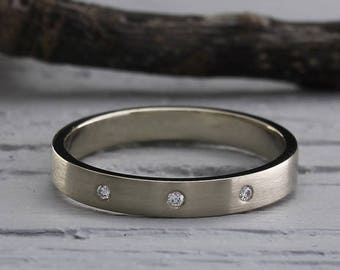 Op de afbeelding: Een eenvoudige zilveren trouwring met drie kleine diamanten die in de band zijn gezet.