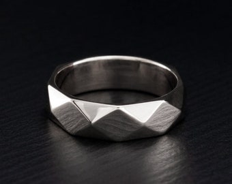 May include: A silver wedding band with a geometric, faceted design. The band is smooth and polished.
