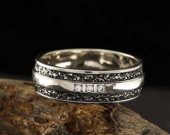 May include: A silver wedding band with a black textured band and three small diamonds.