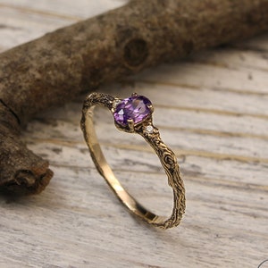 May include: A delicate gold ring with a purple gemstone and small diamonds set in a twig-like band.