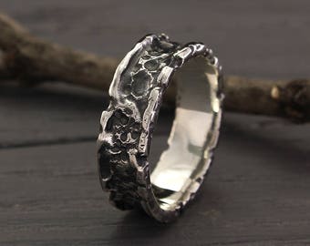 Op de afbeelding: Een zilveren trouwring met een getextureerde, gehammerde afwerking. De ring is breed en heeft een afgerond profiel.