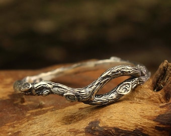 May include: A silver ring shaped like a twisted branch with detailed texture. The ring is resting on a piece of weathered wood.