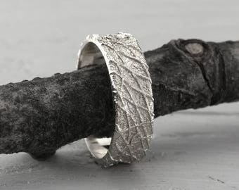 Rustic style man's wedding band in sterling silver with rough surface and shiny finish