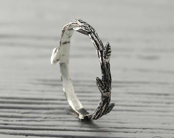 May include: A silver ring featuring a twig design. The ring is crafted from textured metal and has a delicate, natural appearance.